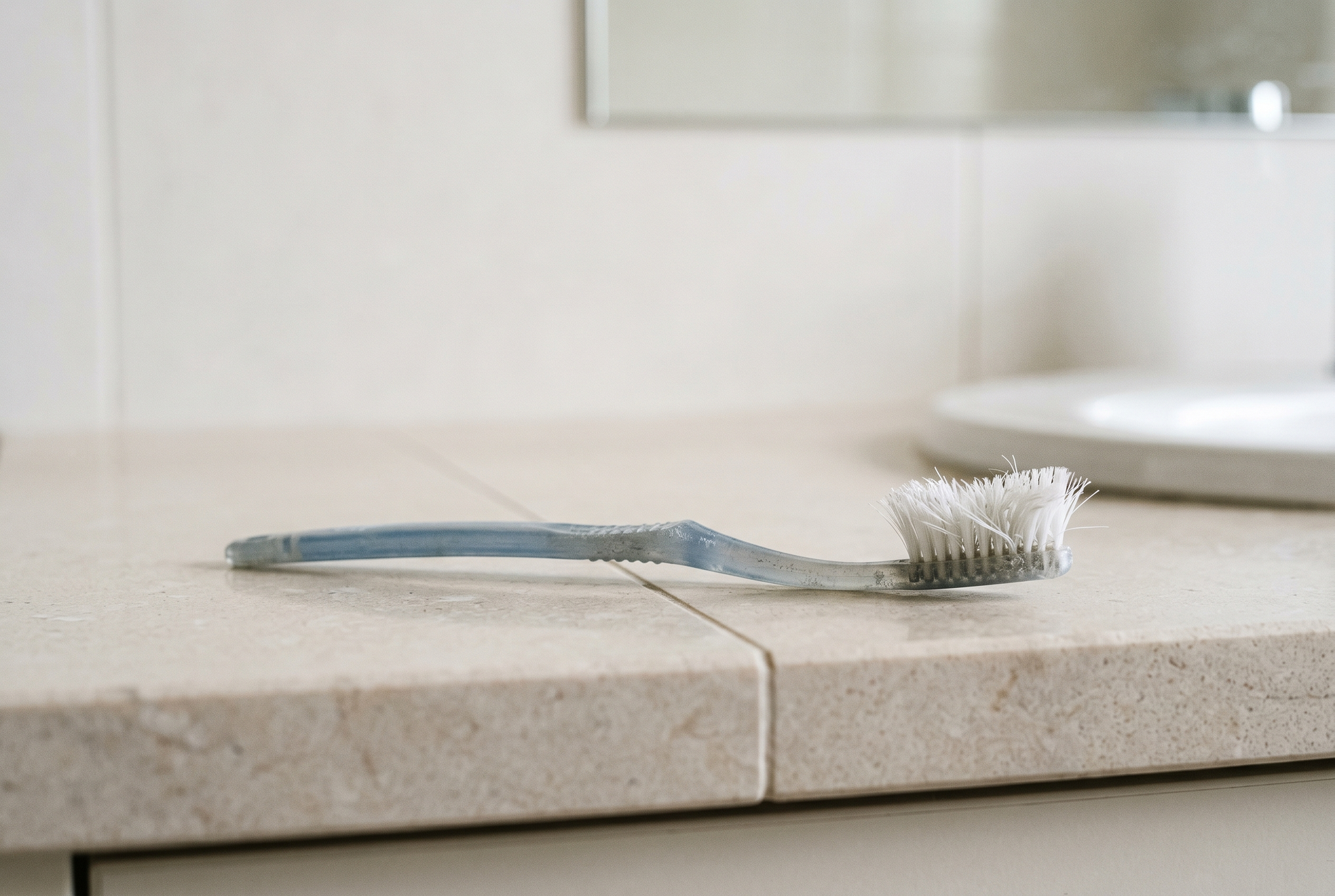 An old worn plastic toothbrush with splayed bristles on a bathroom counter