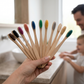A hand offering the set of bamboo toothbrushes to a family in the bathroom