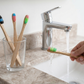 A hand rinsing a bamboo toothbrush while others stand drying in a cup