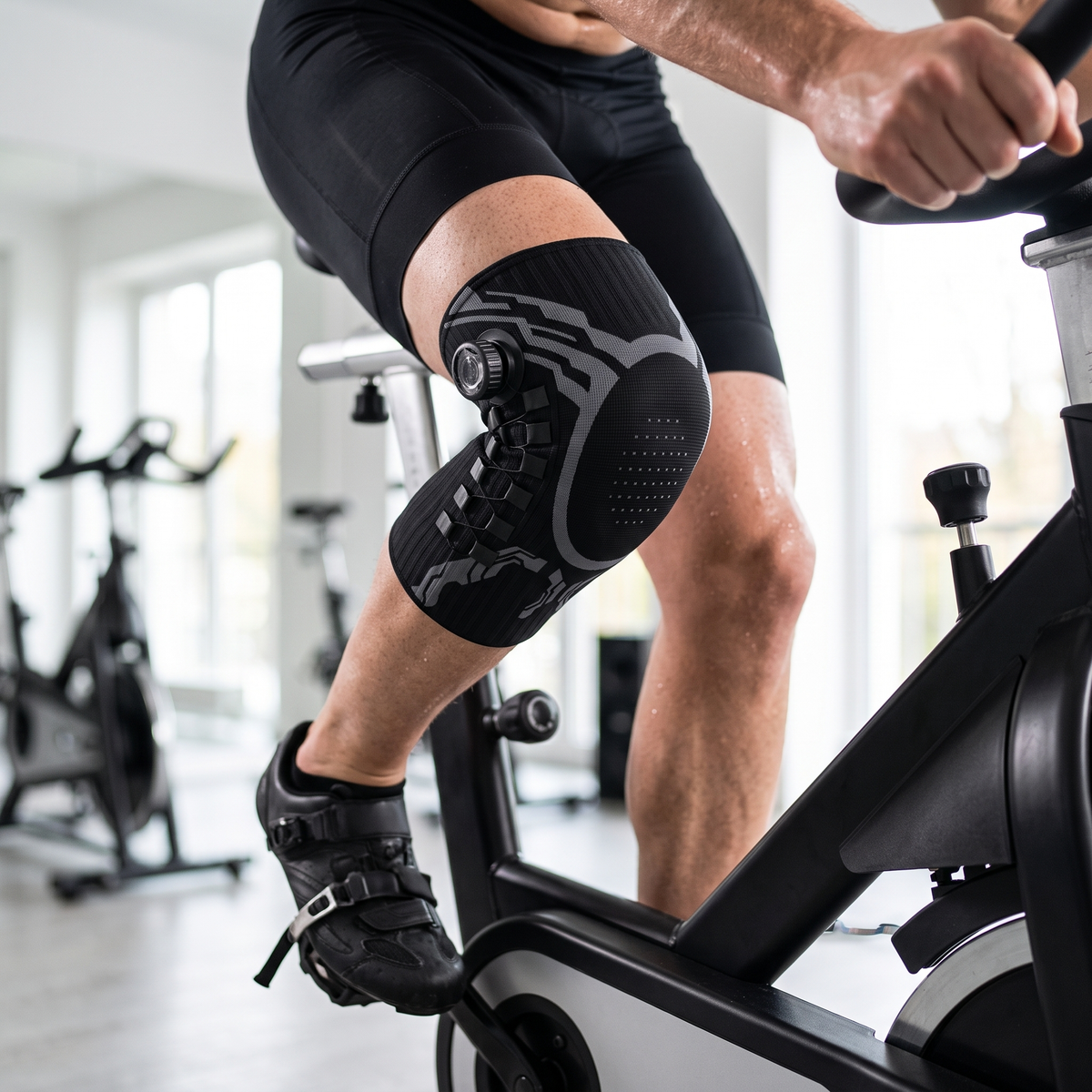 Man cycling indoors wearing the black compression knee sleeve