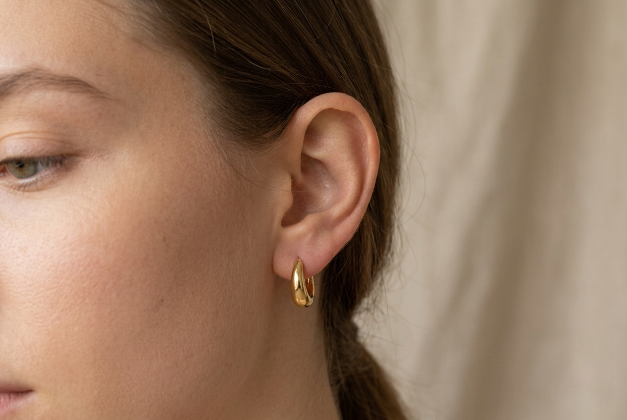 A small gold-tone huggie hoop earring sitting close against the lobe, neat and minimal