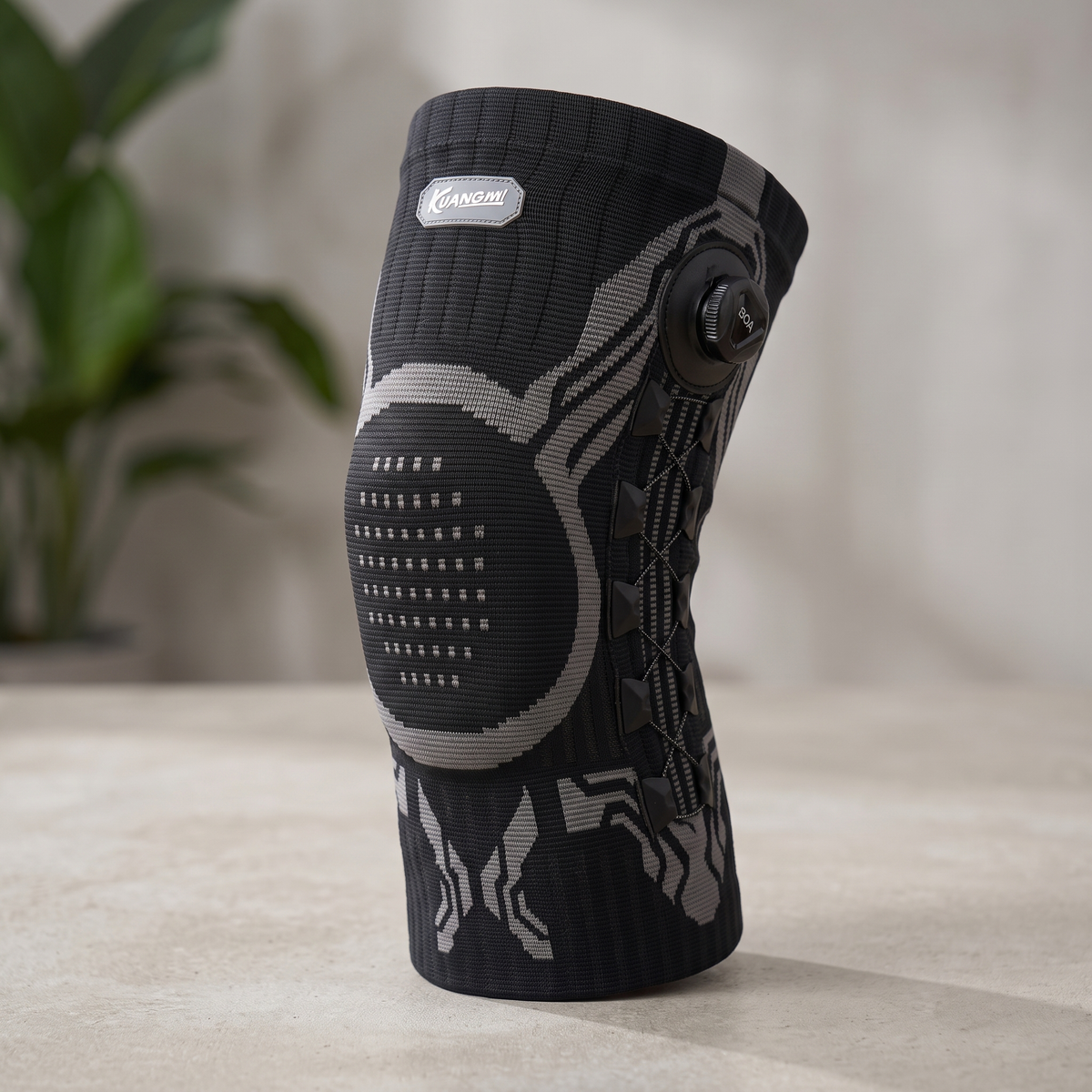 Black KUANGMI knee brace with rotary knob and cross lacing on a clean surface